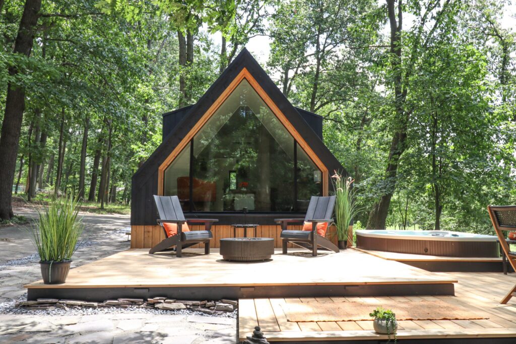 The front of the A-frame, its full-height gable window reflecting the woods